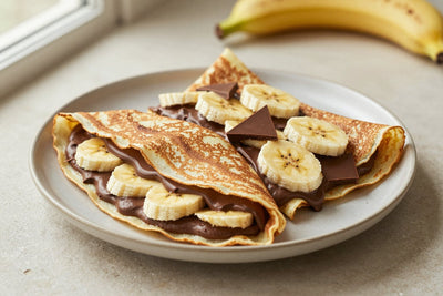 Folded banana chocolate crêpes on a plate, the filling and toppings from the recipe clearly visible