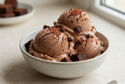 Two generous scoops of brownie batter ice cream in a shallow ceramic bowl, softly melting at the edges