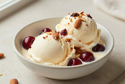 Two generous scoops of cherry almond ice cream in a shallow ceramic bowl, softly melting at the edges