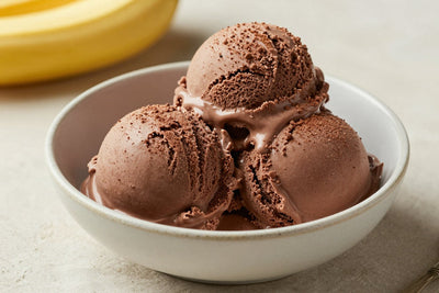 Two generous scoops of chocolate banana ice cream in a shallow ceramic bowl, softly melting at the edges