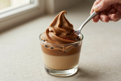 A generous swirl of coffee gelato in a small glass cup with a flat gelato spade