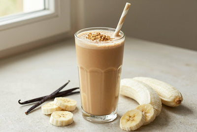 A tall glass of thick, creamy cold brew protein shake with a straw, a few of its fresh ingredients beside it