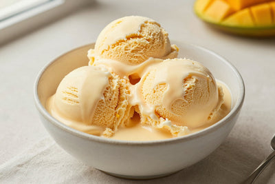 Two generous scoops of mango ice cream in a shallow ceramic bowl, softly melting at the edges