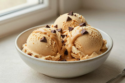 Two generous scoops of peanut butter cup-style ice cream in a shallow ceramic bowl, softly melting at the edges