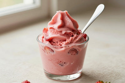 A generous swirl of strawberry gelato in a small glass cup with a flat gelato spade