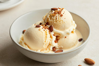 Two generous scoops of almond ice cream in a shallow ceramic bowl, softly melting at the edges