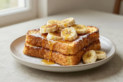 A stack of thick golden slices of banana french toast on a plate, dusted with powdered sugar