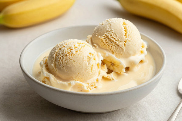 Two generous scoops of banana pudding ice cream in a shallow ceramic bowl, softly melting at the edges