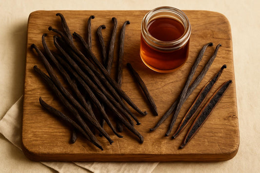 Scattered Grade B Madagascar vanilla beans on a rustic wooden cutting board with a small glass jar of homemade extract and a