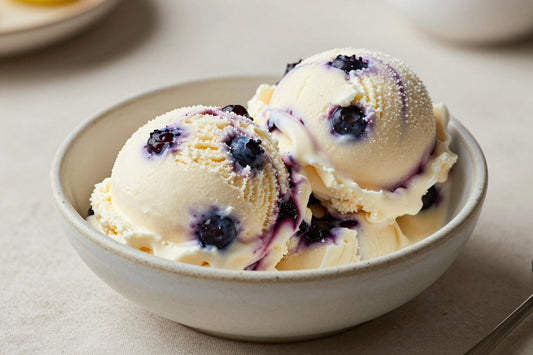 Two generous scoops of blueberry cheesecake ice cream in a shallow ceramic bowl, softly melting at the edges
