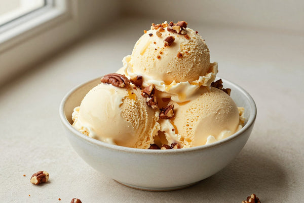 Two generous scoops of butter pecan ice cream in a shallow ceramic bowl, softly melting at the edges