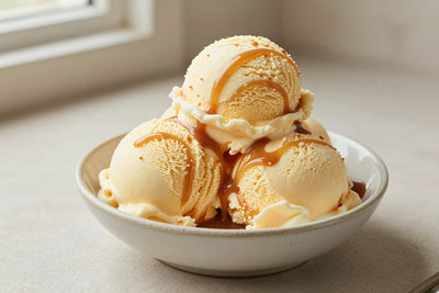 Two generous scoops of caramel swirl ice cream in a shallow ceramic bowl, softly melting at the edges