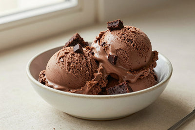 Two generous scoops of chocolate brownie ice cream in a shallow ceramic bowl, softly melting at the edges