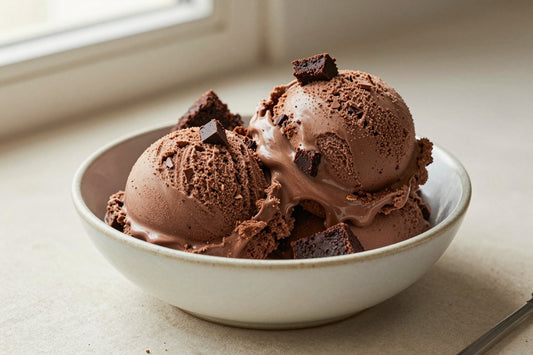 Two generous scoops of chocolate brownie ice cream in a shallow ceramic bowl, softly melting at the edges