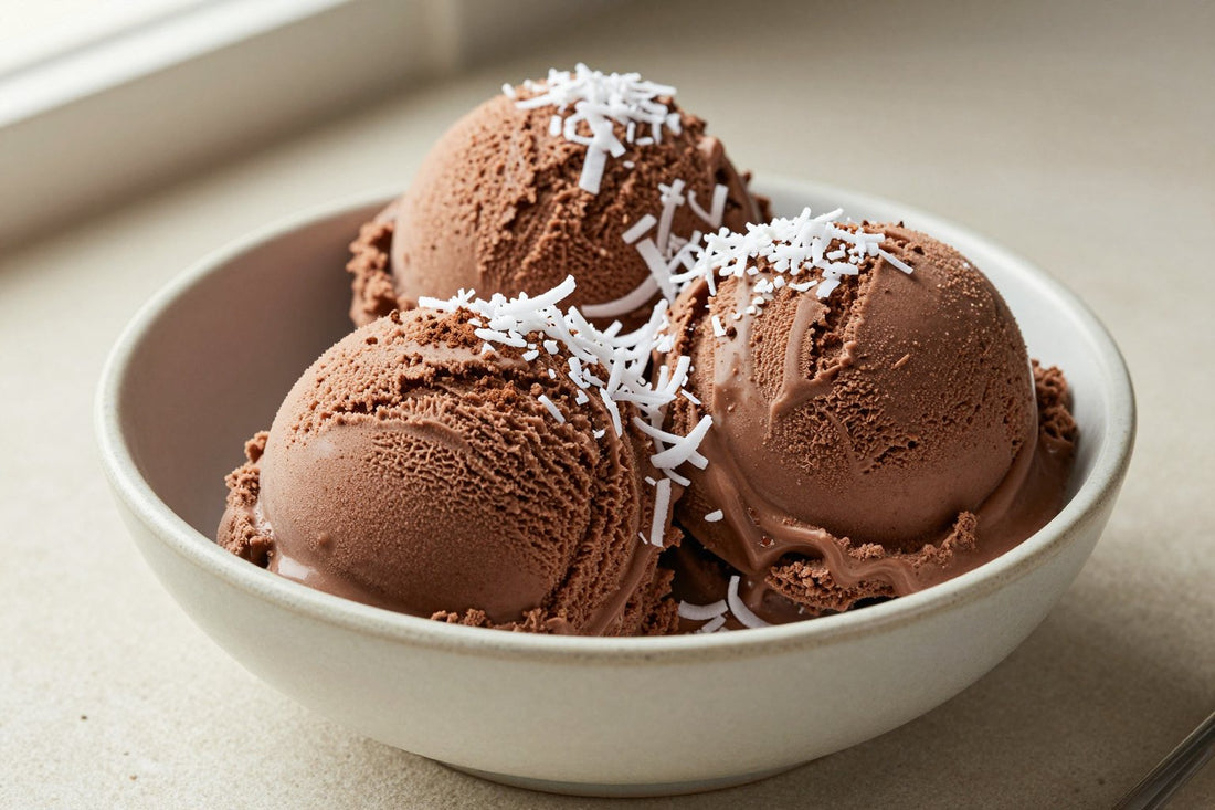 Two generous scoops of chocolate coconut ice cream in a shallow ceramic bowl, softly melting at the edges