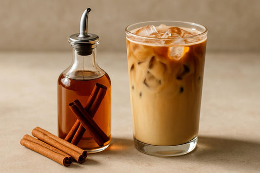A small glass bottle of cinnamon syrup with a pour spout, beside an iced latte sweetened with it