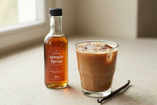 A small glass bottle of classic simple syrup with a pour spout, beside an iced latte sweetened with it