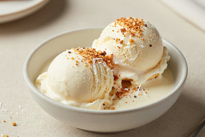 Two generous scoops of coconut cream pie ice cream in a shallow ceramic bowl, softly melting at the edges
