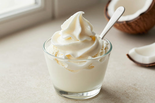 A generous swirl of coconut gelato in a small glass cup with a flat gelato spade