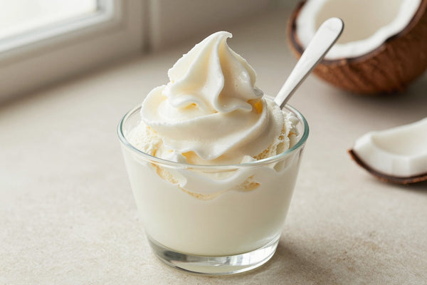 A generous swirl of coconut gelato in a small glass cup with a flat gelato spade