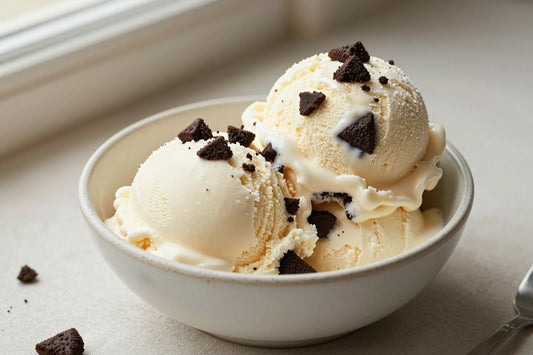 Two generous scoops of cookies & cream ice cream in a shallow ceramic bowl, softly melting at the edges