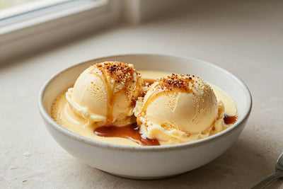 Two generous scoops of crème brûlée ice cream in a shallow ceramic bowl, softly melting at the edges