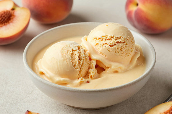 Two generous scoops of fresh peach ice cream in a shallow ceramic bowl, softly melting at the edges
