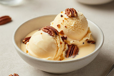 Two generous scoops of maple pecan ice cream in a shallow ceramic bowl, softly melting at the edges