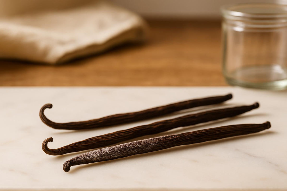 Three Madagascar vanilla beans on a white marble surface, one showing fine white vanillin crystals on the surface, soft