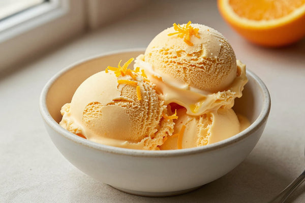 Two generous scoops of orange creamsicle ice cream in a shallow ceramic bowl, softly melting at the edges