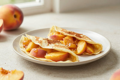 Folded peach crêpes on a plate, the filling and toppings from the recipe clearly visible