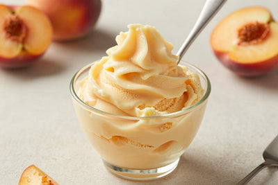 A generous swirl of peach gelato in a small glass cup with a flat gelato spade
