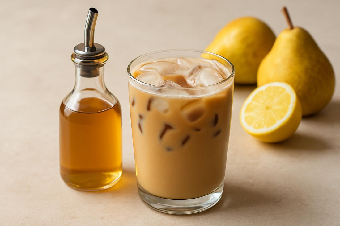 A small glass bottle of pear syrup with a pour spout, beside an iced latte sweetened with it
