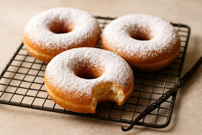Doughnuts finished with powdered sugar dusting on a cooling rack