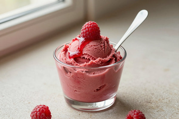 A generous swirl of raspberry gelato in a small glass cup with a flat gelato spade