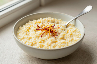 Creamy saffron rice pudding in a small ceramic bowl with a spoon, garnished as in the recipe