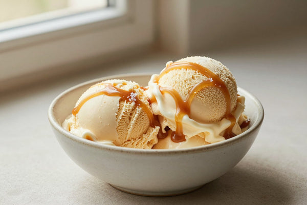 Two generous scoops of salted caramel ice cream in a shallow ceramic bowl, softly melting at the edges