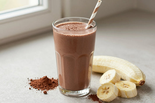 A tall glass of thick, creamy tofu chocolate protein shake with a straw, a few of its fresh ingredients beside it