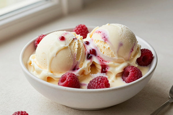 Two generous scoops of white chocolate raspberry ice cream in a shallow ceramic bowl, softly melting at the edges