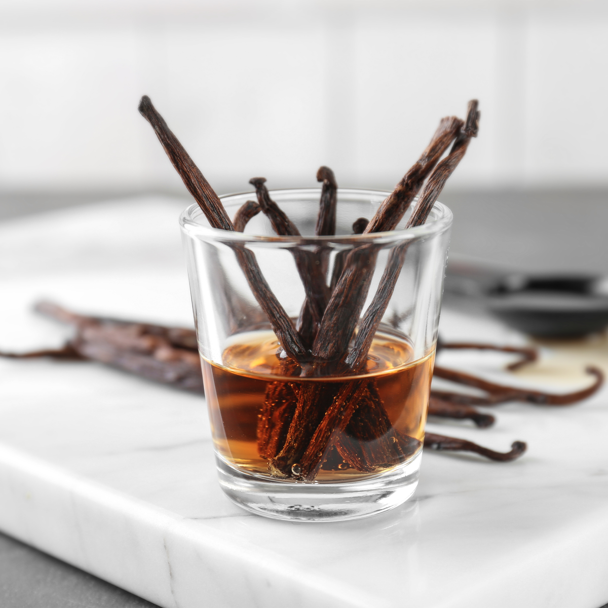 Glass of vanilla extract with vanilla beans on a marble surface
